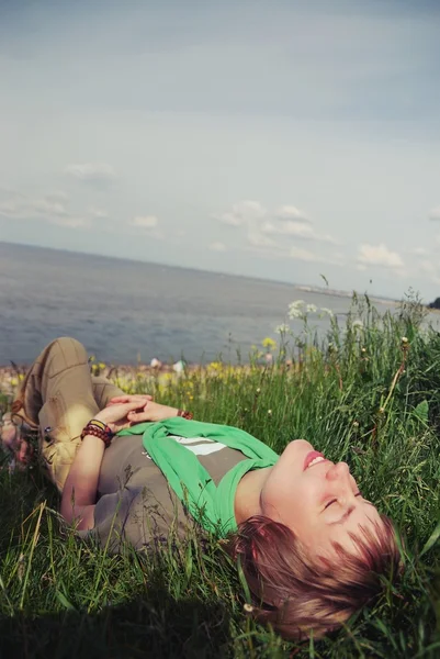 Young beautiful girl lying with her eyes closed and a smile on his face on the green grass on the bay on a warm sunny day