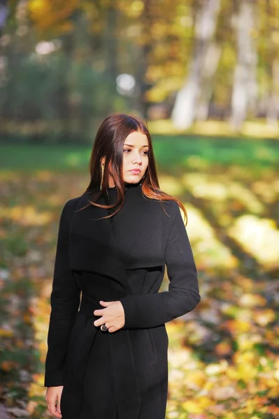 Portrait of a sad, long-haired girl in an elegant black cardigan on sunny day in autumn park.