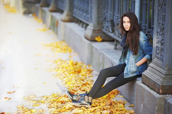 Young pensive brunette girl sitting on a concrete curb around a