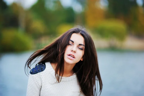 Young beautiful girl with flying in the wind, hair, and eyes veiled by the lake, creating a soft background of the , close-up.