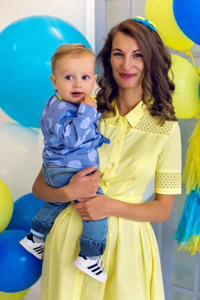 Happy mom in a yellow dress holds  young son in blue clothes