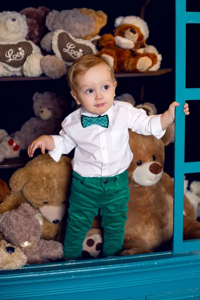 Little child standing on the floor near the Christmas bears in the white shirt and green pants