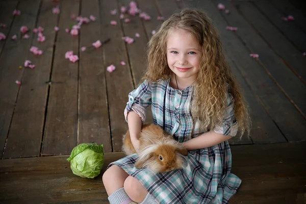 Girl with rabbit sitting on the wooden floor near cabbage in front of a house