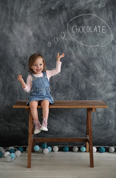 Little girl sitting on the table on the background of black writing wall