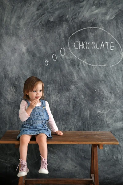 Little girl sitting on the table on the background of black writing wall