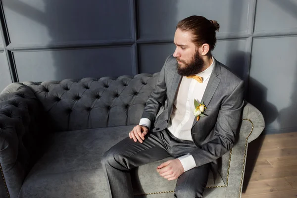Handsome strong, brutal bearded man sitting on the grey sofa