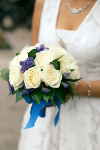 Bride holding wedding bouquet of cream roses and purple flowers with a blue ribbon