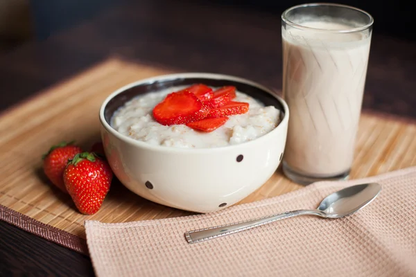 Hot oatmeal, with pieces of strawberries and warm cocoa with milk on a wooden table