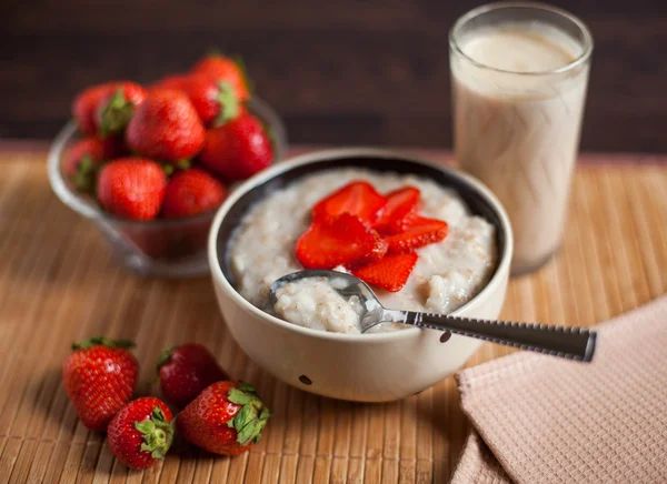 Hot oatmeal, with pieces of strawberries and warm cocoa with milk on a wooden table