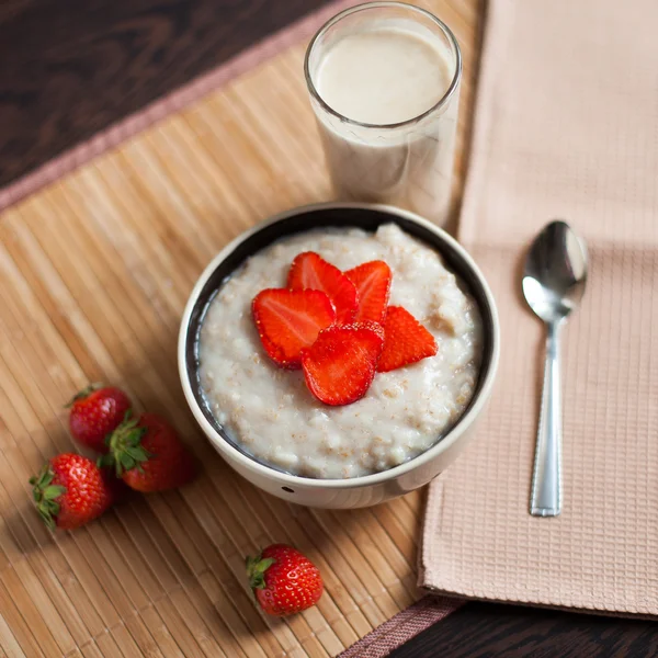 Hot oatmeal, with pieces of strawberries and warm cocoa with milk on a wooden table