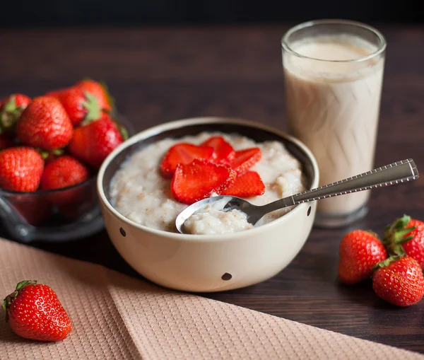 Hot oatmeal, with pieces of strawberries and warm cocoa with milk on a wooden table