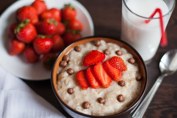 Hot oatmeal, with pieces of strawberries and warm cocoa with milk on a wooden table