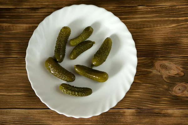 Pickles (pickled cucumber) on a white plate on a wooden background