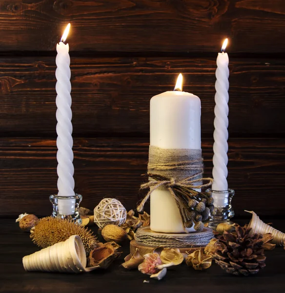 Big white candle and two spiral white candles on rustic wooden background.