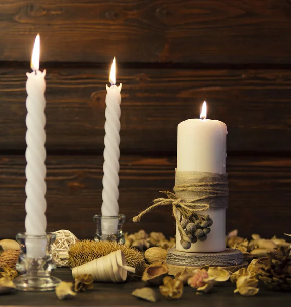 Big white candle and two spiral white candles on rustic wooden background.