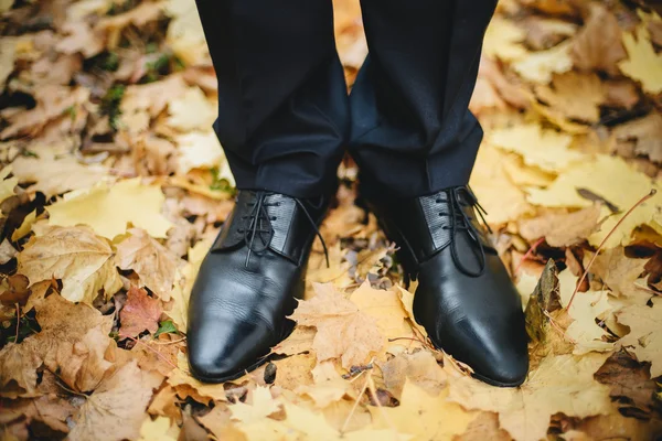 Groom's feet with wedding shoes on the ground in autumn