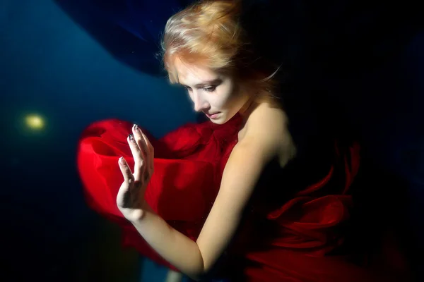 Girl in red dress dancing under water on blue background