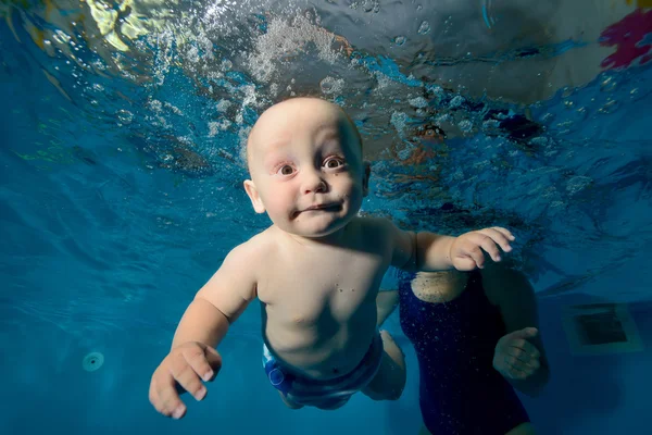 Happy baby infant swims underwater in the pool one on a blue background. Bottom view. Close-up. Horizontal orientation