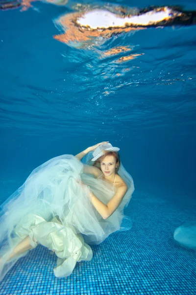 Girl underwater in white wedding dress swims and plays on a blue background
