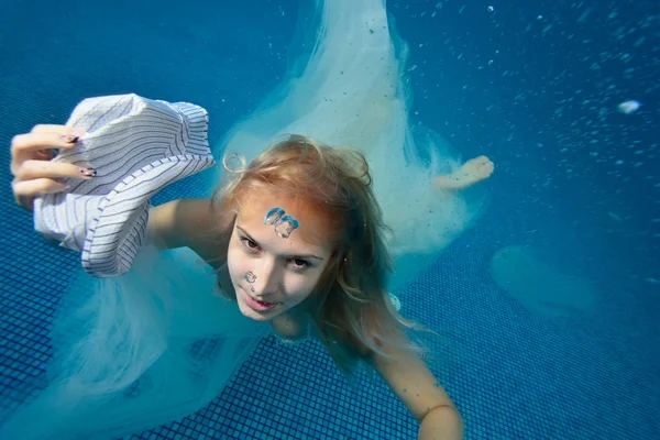 Girl in a white wedding dress POPs up from under the water to the surface and holds a hat in his hand. Top view. Portrait. Close-up.