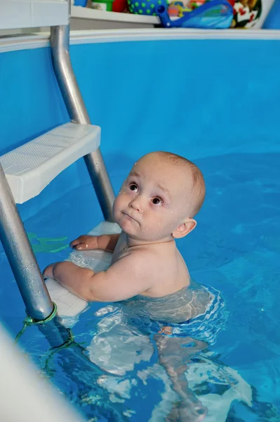 The kid stands on the stairs in the paddling pool and looking up. Close-up. Portrait. The view from the top. Vertical orientation