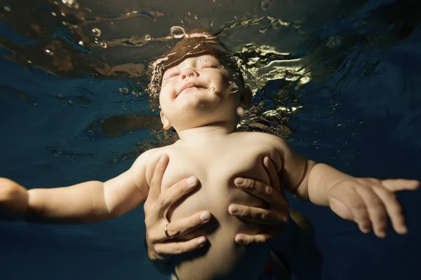 Mother holding baby under water in his hands and helps him to float to the surface of the pool