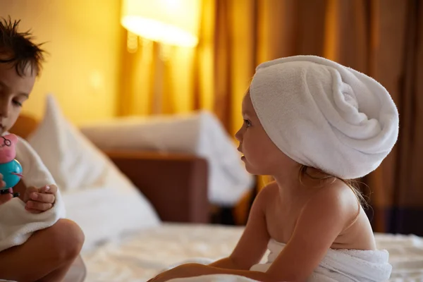 Boy and sister with wet hair under towels over bed