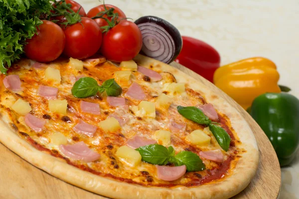 Fresh italian pizza hawaii on wooden board with vegetables, close up