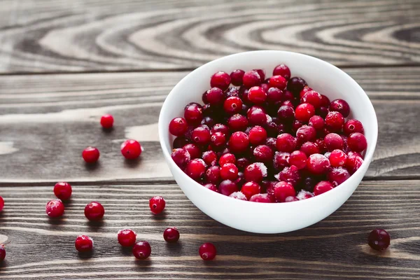 Frozen cranberries in the white dish on a wooden background