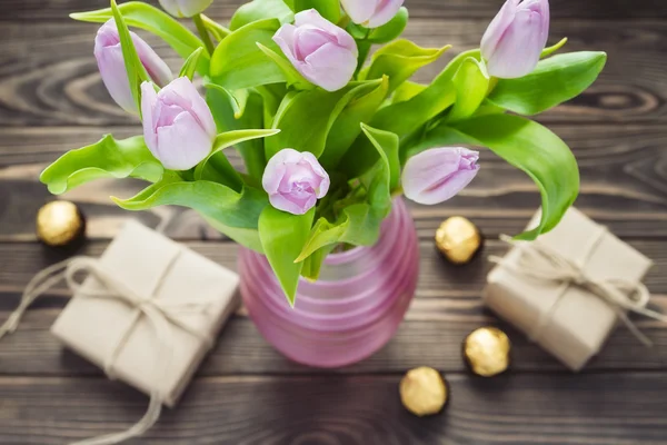 Bouquet of purple tulip in the pink vase with gift boxes and candies