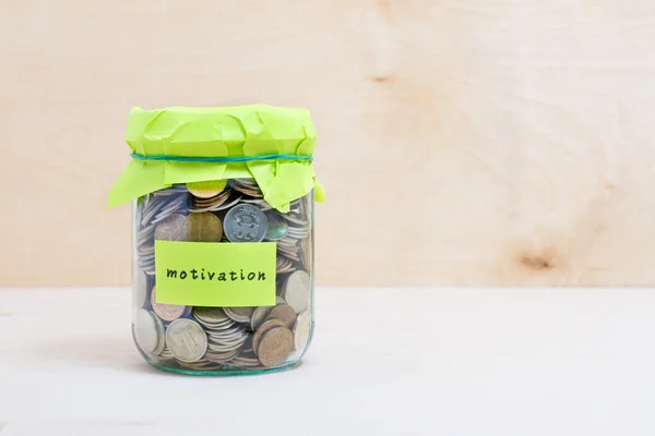Financial concept. Coins in glass money jar with motivation label. Wooden background