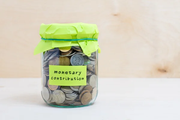 Financial concept. Coins in glass money jar with monetary contribution label. Wooden background