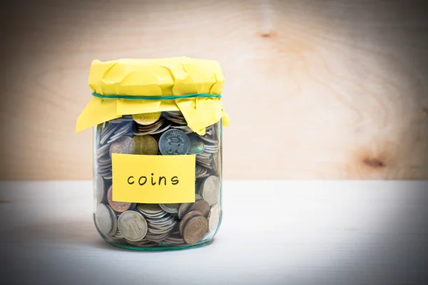 Financial concept. Coins in glass money jar with coins label. Wooden background