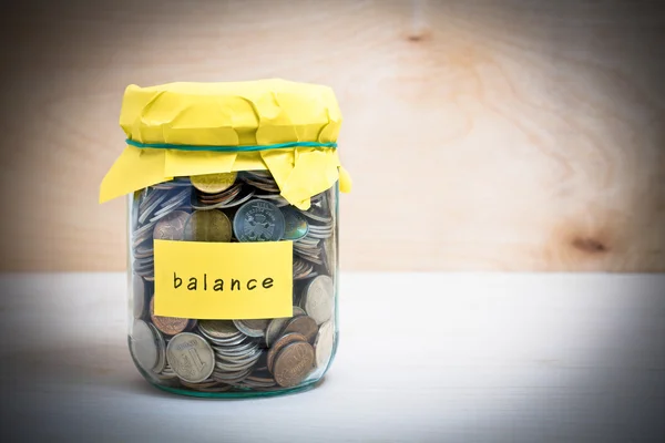 Financial concept. Coins in glass money jar with balance label. Wooden background