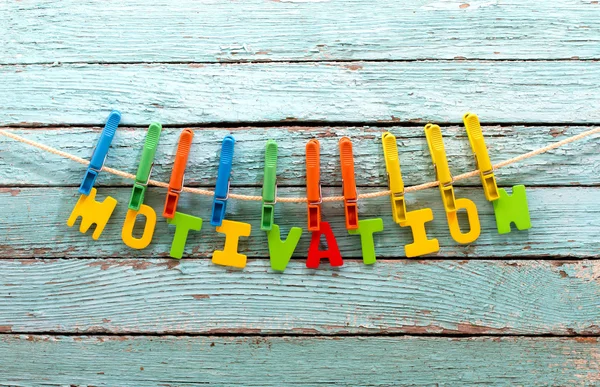 Word motivation fasten clothespins on a rope behind a wooden background