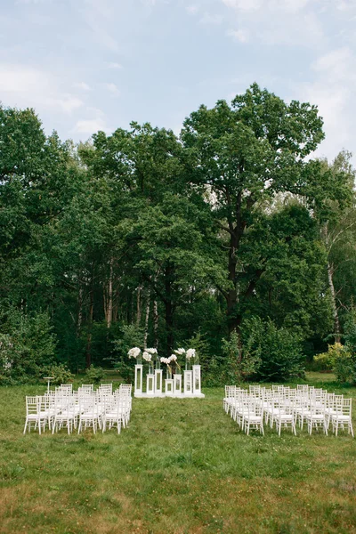 Wedding ceremony in a beautiful garden. white chairs and mirrored tables. Glass vase with flowers calla lilies amaryllis
