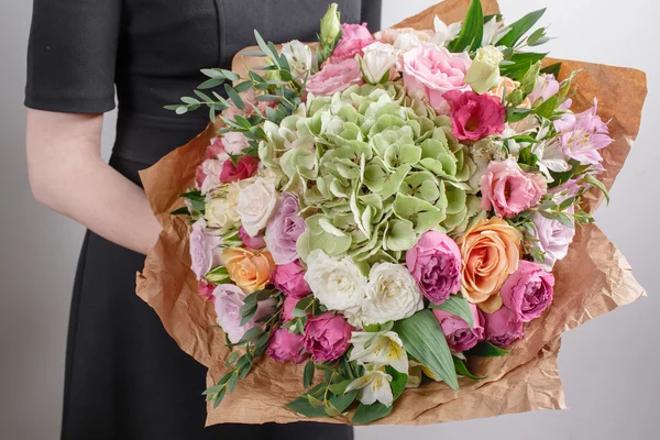 Florist at work. Make hydrangea rich bouquet. Vintage floristic background, colorful roses, antique scissors and a rope on an old wooden table