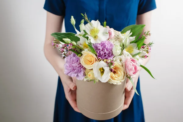 Work florist, bouquet in a round box. smelling flowers holding peach roses in hat against the plastered wall.