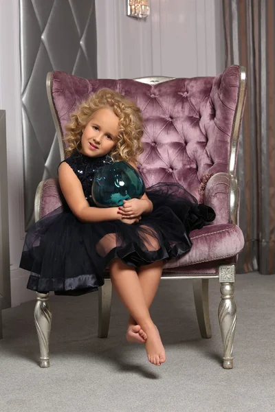 Cute little blond girl sitting in a chair of classic style