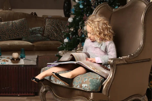 Cute little blond girl sitting on background of Christmas tree