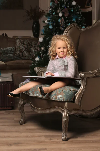 Cute little blond girl sitting on background of Christmas tree