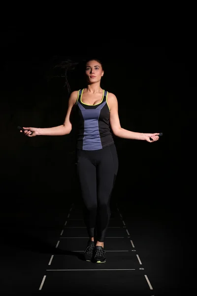 Cute, athletic girl with a skipping rope on black background.