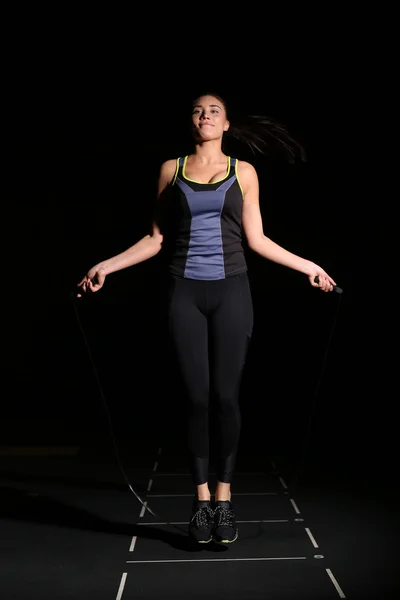 Cute, athletic girl with a skipping rope on black background.