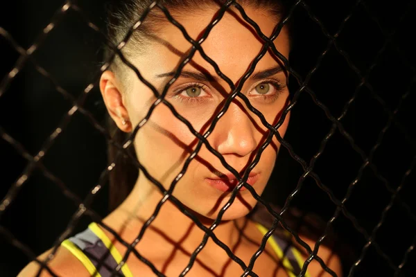 Portrait beautiful fitness girl near fence of grid in gym