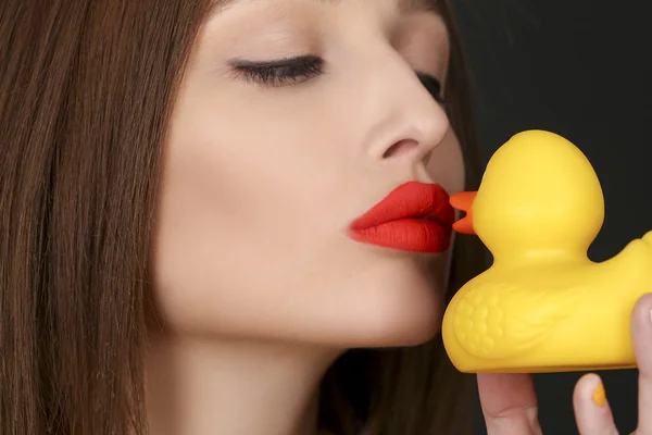 Brunette woman with red lips kissing yellow rubber duck