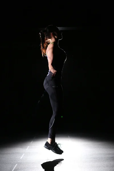 Profile of athletic girl with skipping rope on black background.