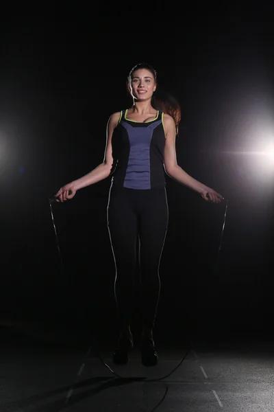 Cute, athletic girl with a skipping rope on black background.