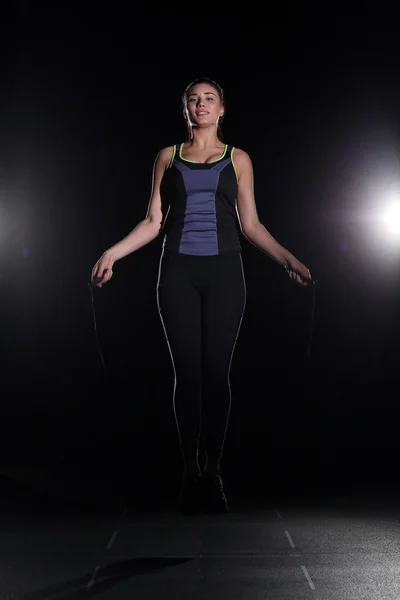 Cute, athletic girl with a skipping rope on black background.