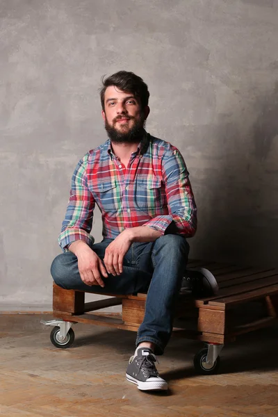 Bearded guy in colorful shirt and jeans sitting with crossed legs