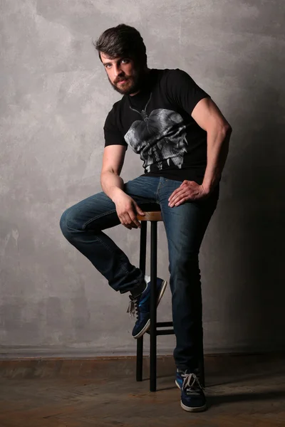 Bearded man sitting on a bar stool. Gray
